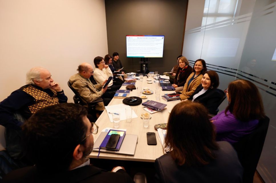 Reunión del Consejo de Evaluación de la Universidad de Chile en una sala de trabajo accesible e iluminada, con académicas y académicos sentados en torno a una mesa rectangular. En la imagen se observa a la prorrectora Alejandra Mizala, Thomas Griggs y profesoras y profesores como Jaime San Martín, Pablo Oyarzún, Jenny Fiedler, Carmen Sotomayor, Maricruz Gómez de la Torre, Verónica Figueroa Huencho y Ana María Madrid, revisando el informe de autoevaluación institucional y los próximos desafíos.